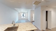 Located at 986 Broadway in Chula Vista, this single-story unit offers a clean, modern aesthetic defined by crisp white walls, recessed lighting, and light-toned hardwood-style flooring that runs throughout the open living area. The layout connects the kitchen and living space seamlessly, creating an airy, functional flow ideal for everyday living.

The kitchen features a standout stone countertop with striking veining in warm neutral tones, paired with a stainless steel sink and contemporary fixtures. A ceiling-mounted HVAC vent ensures efficient climate control, blending discreetly into the white ceiling above.

The living area is bathed in natural light from a large window at the far end, framing a view of the surrounding exterior while keeping the interior bright and welcoming. The entry door includes a narrow sidelight, further enhancing the sense of openness near the foyer.

Throughout the unit, the design maintains a minimalist, move-in-ready character with clean lines, neutral tones, and thoughtful architectural detailing. The overall ambiance is fresh and contemporary, offering a comfortable and well-lit environment in a convenient Chula Vista location.
