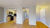 Located at 2450 County Road 28 in Canandaigua, NY, this single-floor unit offers a functional layout across three bedrooms, a living room, a kitchen, and a connecting hallway. Light wood laminate flooring runs throughout the main living areas, complemented by neutral warm-beige walls and textured ceilings, creating a cohesive and understated aesthetic.

The living room is a well-proportioned open space featuring a window that allows natural light to fill the room, alongside a wall-mounted AC unit and baseboard heating. An adjacent room—likely the primary bedroom—features a ceiling fan, a sliding glass door with vertical blinds providing outdoor access, and additional natural light.

The galley-style kitchen is efficiently organized with light wood cabinetry lining both walls, dark granite-style countertops, and black appliances including a range, microwave, refrigerator, and dishwasher. The hallway connects the main living areas to the bedrooms and also houses a stacked washer and dryer unit.

The bedrooms feature plush carpeting, baseboard heating, and windows with blinds. At least one bedroom includes a sliding closet with built-in shelving. The primary bedroom offers a generous footprint, providing comfortable accommodations. Overall, the unit presents a clean, practical living environment.