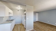 This single-floor unit offers an efficient and functional layout comprising a living room, kitchen, and bathroom. Consistent wood-look flooring runs throughout the space, complemented by cool gray walls and white baseboards that give the interior a clean, cohesive appearance. The textured ceiling adds a classic touch found in each room.

The living area is open and versatile, providing ample room for furnishings, with multiple doors leading to adjacent spaces and a closet. Ceiling-mounted ventilation and recessed lighting fixtures contribute to the room's practical design.

The kitchen features a galley-style layout with white upper cabinetry, a double-basin sink with light-toned countertops, and white appliances including a refrigerator and range. A structural beam detail at the kitchen entrance adds architectural character, while a flush-mount ceiling light illuminates the workspace.

The bathroom is finished with a white full-length tub and shower surround, complemented by chrome fixtures, offering a straightforward and clean bathing area.

Overall, the space maintains a neutral, move-in-ready aesthetic with a consistent color palette, making it well-suited for a variety of furnishing styles. The layout maximizes the use of the available footprint across all three rooms.