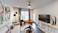 This single-floor residence showcases a cohesive modern design with carefully selected finishes across all rooms. The kitchen is a standout space, featuring two-tone cabinetry combining white gloss upper cabinets with wood-grain lower units, white quartz countertops, a full suite of stainless steel appliances, a tile backsplash with under-cabinet lighting, and a large island with an integrated sink. Stylish pendant lights illuminate the workspace, adding a contemporary touch.

The living area offers dark hardwood-style flooring, large windows with patterned drapes that allow natural light to filter in, a ceiling fan, and a private exterior door. Multiple bedrooms feature plush carpeting, ceiling fans, and large windows with outdoor views. At least one bedroom includes a walk-in closet and direct bathroom access.

The bathrooms are finished in a clean, minimalist style. One features an LED-backlit mirror, a sleek floating vanity, dark hardwood-style flooring, and a separate soaking tub. A secondary bathroom includes a full tub-shower combination, white cabinetry, and wood-tone door accents consistent with the overall design language of the home.