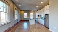 This single-floor, 2-bedroom, 2-bathroom residence in Memphis, Tennessee, blends industrial character with contemporary finishes throughout its well-organized layout. The open-concept living and kitchen area serves as the heart of the unit, anchored by polished concrete floors that reflect natural light streaming in through multiple large, white-trimmed windows. Exposed conduit piping runs along the upper walls and ceiling, lending the space an industrial loft aesthetic that contrasts with the clean, modern kitchen design.

The kitchen is outfitted with high-gloss white cabinetry extending to the ceiling, a pale blue glass tile backsplash, dark gray countertops, stainless steel appliances including a refrigerator and dishwasher, and a central island that provides additional prep and storage space. Recessed lighting supplements the abundant natural light throughout.

The two bedrooms offer a quieter atmosphere; one features polished concrete flooring while the other is carpeted, and both provide access to well-appointed bathrooms. The bathrooms are finished with hexagonal penny-tile floors, wood-toned vanity cabinetry, light quartz countertops, and white subway tile surrounding the tub and shower enclosures. Outdoor views of surrounding greenery are visible through the generously sized windows, enhancing the overall brightness and openness of the space.