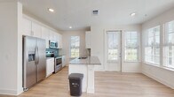 This single-story residence in Jacksonville, FL (32256) offers a clean, contemporary design with consistent finishes throughout. The open-concept kitchen serves as a central highlight, featuring white shaker-style cabinetry, granite countertops, and a teal glass tile backsplash. Stainless steel appliances—including a French door refrigerator, range, and microwave—complement the modern aesthetic. A peninsula with an undermount sink and additional counter seating enhances both functionality and flow into the living area. Light wood-tone flooring runs continuously throughout the space, creating a cohesive and airy feel.

Multiple windows fitted with horizontal blinds allow generous natural light and offer views of the surrounding greenery. The living area is well-proportioned and includes a ceiling fan, while a secondary room mirrors this layout with its own set of windows and ceiling fan.

The bathrooms maintain the same refined finishes, with granite-topped white vanities and wood-tone flooring. The primary bathroom features a glass-enclosed walk-in shower, while a secondary bathroom includes a shower-tub combination. The floorplan model reveals a well-organized layout with clearly defined living, sleeping, and utility zones.