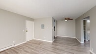 This single-floor unit presents a clean, updated interior finished in a neutral grey and white palette throughout. Light grey vinyl plank flooring runs continuously across all rooms, lending a cohesive and modern feel to the space. The open living area is well-lit, benefiting from a large sliding glass door dressed with vertical blinds that allows natural light to fill the room. A wall-mounted air conditioning unit and baseboard heaters provide year-round climate control.

The entry area includes a front door panel and electrical box, flowing naturally into the living space, which is further complemented by a ceiling fan. The galley-style kitchen is efficiently laid out with white cabinetry on both sides, granite-patterned countertops, and white appliances including a refrigerator and dishwasher.

The bedrooms are generously proportioned, each featuring baseboard heating, natural window light, and closet space with built-in shelving. One bedroom includes a wall-mounted air conditioning unit and access to the patio. The bathroom is neatly appointed with a white vanity featuring ample cabinet storage, granite-style countertop, a large mirror, and a full tub-shower combo. Overall, the space offers a clean, functional, and well-maintained environment.