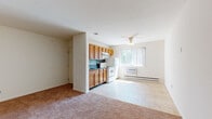 This single-floor residence offers a practical and functional layout with well-defined living spaces. The open-plan living and dining area is finished with plush carpeting and features a ceiling fan with light fixture, a baseboard heater, and a wall-mounted air conditioning unit, ensuring year-round comfort. A large window allows natural light to fill the space, creating a bright and inviting atmosphere.

The kitchen is thoughtfully appointed with warm honey-toned wooden cabinetry offering generous upper and lower storage, dark countertops, and a dark tile backsplash. White appliances, including a freestanding electric range with overhead ventilation, a refrigerator, and a sink, provide all the essentials. Light tile flooring ties the kitchen and living area together seamlessly.

The bedroom is a generously sized, carpeted retreat featuring two side-by-side sliding-door closets, offering ample storage. A window provides natural light and ventilation, while a baseboard heater ensures warmth throughout the season.

The bathroom is clean and straightforward, featuring white tile flooring, a full-sized bathtub with a white tiled surround and overhead shower, a toilet, and a vanity with sink. The space is finished in neutral tones, contributing to an overall sense of simplicity and functionality throughout the unit.
