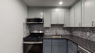 Located in Quincy, MA, this thoughtfully renovated single-floor unit delivers a clean, modern aesthetic across every room. The open living area is finished with durable wood-look plank flooring, crisp white walls, recessed lighting, and baseboard heating — creating a bright, welcoming atmosphere. A sliding glass door brings in natural light and adds a sense of openness to the space.

The kitchen is a true standout, showcasing a two-tone cabinet design with sage-gray uppers and slate-blue lowers, all topped with dark granite countertops. A herringbone tile backsplash adds visual texture, while stainless steel appliances — including a gas range, over-the-range microwave, and refrigerator — complete the space with a polished, contemporary finish.

The bedrooms continue the cohesive design language, featuring the same wood-look flooring, recessed lighting, and neutral white walls. One bedroom includes a closet with built-in shelving and natural light from a window, while another offers additional closet storage. Baseboard heating is present throughout for year-round comfort.

The bathroom is finished with large-format neutral tile in the tub surround and on the floor, complemented by chrome fixtures, a granite vanity top, and a classic soaking tub — offering a clean, spa-like feel. Overall, this unit presents a cohesive, move-in-ready interior with modern upgrades throughout.