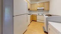 This single-floor residence offers a practical and well-organized layout designed to maximize comfort and functionality. The spacious living area is finished with wall-to-wall carpet and features a textured ceiling, a ceiling fan, and a sliding glass door that opens onto a private balcony with outdoor views — filling the room with natural light. The front entry door opens directly into this generous living space, creating an inviting and open feel.

The kitchen is efficiently arranged in an L-shaped configuration and features light wood cabinetry offering ample storage, white appliances including a refrigerator, electric range, and dishwasher, and light hardwood-style flooring that adds warmth to the space. A range hood is installed above the cooktop for ventilation.

The carpeted bedroom area is quiet and comfortable, with a ceiling fan providing airflow and direct access to the adjoining spaces. The bathroom is clean and straightforward, featuring a full-size soaking tub with shower combination, a window with blinds for natural light and privacy, hardwood-style flooring, and a vanity sink. The overall aesthetic throughout the unit is neutral and bright, with white walls and light finishes that create a cohesive and move-in-ready environment.