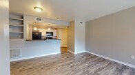 This single-floor residence features a practical and cohesive layout designed for comfortable everyday living. The open-concept living area is finished with wood-look plank flooring in a warm gray tone and neutral gray walls accented by clean white baseboards, creating a bright and versatile space. A peninsula-style kitchen overlooks the living area, offering dark granite-style countertops, white cabinetry, and a full suite of black appliances including a refrigerator, electric range, and over-the-range microwave. Pendant lighting above the peninsula adds a functional decorative touch.

The bedrooms are carpeted for comfort, each offering closet storage. One bedroom features a walk-in closet, while the other includes a standard sliding-door closet and a glass slider door opening to a private balcony with outdoor views. A ceiling fan with lighting is present in one bedroom, enhancing airflow and comfort.

Two bathrooms serve the unit, each with wood-look flooring, white vanities, and neutral gray walls. One bathroom features a tiled shower-tub combination, while the other is appointed with a vanity, mirror, and essential fixtures. The overall ambiance throughout is clean, neutral, and move-in ready.