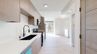 Located on the fifth floor at 154 S Occidental Blvd in Los Angeles, this one-bedroom, one-bathroom unit offers a clean, contemporary design tailored for modern urban living. Light-toned hardwood flooring flows throughout the open layout, creating a cohesive and airy atmosphere that maximizes the sense of space.

The kitchen is a standout feature, outfitted with flat-front warm wood cabinetry, white quartz countertops, and a full suite of stainless steel appliances including a refrigerator, electric range, built-in microwave, and a distinctive teal dishwasher. A matte black dual-basin sink with a flexible pull-down faucet adds a refined, contemporary touch. The kitchen opens directly into the living area, which benefits from a large picture window framing views of a palm tree and the surrounding neighborhood, flooding the space with natural light.

The living area is bright and versatile, with recessed lighting and access to a private balcony through sliding glass doors that offer additional city views. The bedroom and hallway connect seamlessly via a warm wood-toned door, maintaining a consistent design language throughout.

The bathroom features a walk-in shower adorned with herringbone white tile walls and a mosaic tile floor, complemented by chrome fixtures for a polished finish. Clean white walls and recessed lighting complete the minimal, modern aesthetic of this well-appointed Los Angeles residence.
