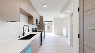 Located on the fifth floor at 154 S Occidental Blvd in Los Angeles, this one-bedroom, one-bathroom unit offers a clean, contemporary design tailored for modern urban living. Light-toned hardwood flooring flows throughout the open layout, creating a cohesive and airy atmosphere that maximizes the sense of space.

The kitchen is a standout feature, outfitted with flat-front warm wood cabinetry, white quartz countertops, and a full suite of stainless steel appliances including a refrigerator, electric range, built-in microwave, and a distinctive teal dishwasher. A matte black dual-basin sink with a flexible pull-down faucet adds a refined, contemporary touch. The kitchen opens directly into the living area, which benefits from a large picture window framing views of a palm tree and the surrounding neighborhood, flooding the space with natural light.

The living area is bright and versatile, with recessed lighting and access to a private balcony through sliding glass doors that offer additional city views. The bedroom and hallway connect seamlessly via a warm wood-toned door, maintaining a consistent design language throughout.

The bathroom features a walk-in shower adorned with herringbone white tile walls and a mosaic tile floor, complemented by chrome fixtures for a polished finish. Clean white walls and recessed lighting complete the minimal, modern aesthetic of this well-appointed Los Angeles residence.