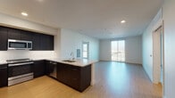Located at 1101 N Main St in Los Angeles, CA, this modern single-floor residence showcases a clean, contemporary design with light wood-style flooring and a bright, neutral color palette throughout. The open-concept layout seamlessly connects the kitchen, dining, and living areas, creating a spacious and functional flow. The kitchen is well-appointed with dark espresso cabinetry, light quartz countertops, stainless steel appliances including a range, built-in microwave, dishwasher, and refrigerator, along with a white subway tile backsplash and a peninsula that provides additional prep and seating space. The living area extends toward a sliding glass door that opens to a private balcony, offering views of the surrounding Los Angeles cityscape and filling the space with natural light. The bedrooms are generously sized, with one featuring a large walk-in closet with built-in shelving and another with a tall window framing outdoor views. The bathrooms are finished in a crisp, all-white palette with dark vanity cabinetry, white quartz countertops, large mirrors, and a soaking tub with shower combination. Recessed lighting throughout the unit enhances the clean, modern aesthetic of this well-designed Los Angeles residence.
