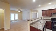 This single-floor residence offers a thoughtfully designed open-concept layout that seamlessly connects the living, dining, and kitchen areas. The spacious living room is anchored by a fireplace and ceiling fan, with natural light streaming in through a set of French doors that open to the outdoors. Plush carpeting throughout the living and bedroom areas adds warmth and comfort to the space.

The kitchen is a functional highlight, featuring rich dark cherry wood cabinetry with brushed nickel hardware, granite-style laminate countertops, a double-basin sink, and black appliances including a coil-top electric range and refrigerator. A raised breakfast bar provides a natural division between the kitchen and living area while maintaining the open feel of the space.

The bedroom is generously sized with soft carpet flooring, a ceiling fan with light fixture, and a window that allows for natural light. The full bathroom is well-equipped with a vanity featuring matching dark wood cabinetry, a framed mirror, tile flooring, a wall-mounted storage cabinet, and a full soaking tub with shower. A dedicated in-unit laundry area houses a full-size washer and dryer, adding everyday convenience. The neutral warm-toned walls throughout create a cohesive and inviting ambiance.