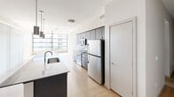 Located at 290 E Roosevelt St in the heart of Phoenix, AZ, this modern one-bedroom, one-bathroom residence offers a well-designed single-floor layout with a clean, contemporary aesthetic. The open-concept kitchen and dining area serves as the centerpiece of the home, showcasing stainless steel appliances including a refrigerator, electric range, and microwave. Dark, textured cabinetry lines the walls and pairs with light quartz countertops, while a large island with an undermount sink provides additional prep space and casual seating. Light wood-tone flooring runs throughout the main living areas, enhancing the bright, airy feel. The living area benefits from expansive floor-to-ceiling windows dressed with vertical blinds, flooding the space with natural light and offering open views of the surrounding Phoenix cityscape. A ceiling fan adds to the comfort of the room. The generously sized bedroom features plush carpeting, a ceiling fan, wide windows with blinds for natural light and privacy, and a dedicated closet with built-in shelving. The bathroom is thoughtfully appointed with a dark wood floating vanity, light countertop, large mirror with overhead lighting, and wood-tone tile flooring. This well-appointed residence blends modern design with functional living in a prime urban location.