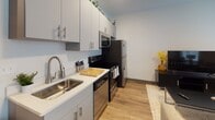 Located at 231 E Washington St in downtown Sandusky, Ohio, this single-floor studio offers a thoughtfully designed open-concept layout that efficiently combines living, sleeping, and dining areas into one cohesive space. Light wood-tone flooring runs throughout, lending warmth and visual continuity across every zone.

The kitchen is well-appointed with sleek grey cabinetry extending to the ceiling, white quartz countertops, a stainless steel sink, and a full suite of stainless steel appliances including a refrigerator, range, dishwasher, and microwave. The galley-style configuration maximizes functionality without sacrificing style.

The main living area is bright and airy, benefiting from multiple large windows that allow generous natural light to fill the space. The open floor plan accommodates both a comfortable seating arrangement and a dedicated sleeping area, along with space for a desk — making it well-suited for both relaxation and productivity.

The bathroom is a standout feature, finished with large-format dark wood-look wall tiles in the walk-in shower, a frameless glass enclosure, wood-tone vinyl flooring, and a modern vanity with a white countertop. The overall design aesthetic throughout the unit is clean, contemporary, and move-in ready.