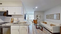 This thoughtfully designed single-floor residence offers a seamless blend of modern aesthetics and functional living. The open-concept layout connects the kitchen and living area, creating a bright and inviting atmosphere enhanced by recessed lighting and light-toned wood-look flooring throughout.

The galley-style kitchen is a standout, featuring white shaker cabinetry with gold hardware, striking granite countertops, a classic white subway tile backsplash, and stainless steel appliances including a gas range, dishwasher, and refrigerator. A deep stainless steel sink with a modern faucet completes the well-appointed space.

The adjacent living area is warm and welcoming, with neutral walls that complement the mid-century modern furnishings. A large window draws in natural light, while a round decorative mirror and wall art add character and depth to the room. A generous closet provides ample storage.

The bedroom is a calm retreat, featuring large windows fitted with blinds, recessed lighting, and continued wood-look flooring. The space feels airy and restful, ideal for unwinding at the end of the day.

The bathroom offers a full tub-shower combination with floor-to-ceiling tile surround in soft gray tones, providing a clean and polished finish. A dedicated in-unit laundry area with a front-loading washer adds everyday convenience to this well-rounded space.