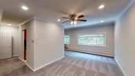 Located at 427 Main Street in Northport, NY, this single-floor residence at Fairfield Northport Village offers a well-organized layout with thoughtfully finished interiors throughout. The main living area is generously proportioned, featuring plush wall-to-wall carpeting, soft gray walls, and crown molding that adds a refined architectural detail. Recessed lighting and a ceiling fan with an integrated light fixture provide both ambient illumination and air circulation, while a bank of windows along the far wall invites natural light and frames views of the surrounding greenery.

The kitchen is efficiently designed with warm wood cabinetry, dark granite countertops, tile flooring, and full appliances including a refrigerator. A doorway from the kitchen leads to a carpeted area with a closet, offering additional storage. The bedroom is a comfortable, well-lit space with carpeting, crown molding, a ceiling fan, a window overlooking lush outdoor foliage, and a wall-mounted HVAC unit. The bathroom features a tub-shower combination enclosed by a sliding glass door, white tile surround with accent detailing, and a vanity with dark granite countertop. Throughout, the unit maintains a clean, neutral aesthetic with consistent finishes.
