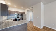 Located at 3837–3885 N Old Missouri Rd in Fayetteville, Arkansas, this single-floor unit offers a well-designed layout with a cohesive mix of modern finishes throughout. The kitchen serves as a functional centerpiece, featuring dark wood cabinetry, granite countertops, a stainless steel appliance suite including a refrigerator, range, microwave, and dishwasher, and a peninsula island that provides additional prep and serving space. Warm-toned hardwood-style flooring runs through the main living and kitchen areas, lending continuity and a clean aesthetic. The living area benefits from natural light and access to a patio through double French doors. Multiple bedrooms are finished with plush carpet, ceiling fans with integrated lighting, and windows that bring in natural light. The primary bedroom connects directly to a private bathroom. The bathrooms are appointed with dark wood vanities, white countertops, round framed mirrors, and stylish vanity lighting, complemented by hardwood-style flooring. A secondary bathroom includes a shower enclosure and additional wall-mounted cabinetry for storage. The overall design palette of neutral tones, dark wood accents, and modern fixtures creates a clean, contemporary ambiance throughout the space.