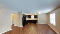 This single-story residence offers a thoughtfully designed floor plan featuring two bedrooms and two bathrooms across a generously sized living area. The open-concept layout seamlessly connects the kitchen and living space, creating a bright and functional environment. The kitchen is appointed with rich, dark espresso cabinetry that provides ample storage, complemented by black appliances including a full-size refrigerator, range, built-in microwave, and dishwasher. A sink positioned beneath a window allows for natural light while preparing meals. The kitchen flows naturally into the expansive living area, which is finished with warm wood-tone laminate flooring that extends throughout the main living space, adding a sense of continuity and warmth. Neutral-toned walls and recessed lighting keep the space feeling clean, bright, and welcoming. A dedicated laundry area is conveniently accessible, adding to the home's practical appeal. The overall ambiance is modern yet comfortable, with a neutral palette that provides a versatile backdrop for a variety of interior styles. This well-appointed residence is an excellent option for those seeking a move-in-ready home with functional design and quality finishes throughout.