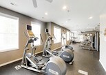 The fitness center at Legacy Pointe Apartments, located at 2901 Legacy Pointe Way in Knoxville, TN, is a well-equipped, single-floor facility designed to support a comprehensive workout routine. The space is thoughtfully laid out to accommodate both cardio and strength training needs, offering residents a convenient on-site exercise option.

The cardio zone features a row of Precor elliptical trainers and treadmills, each equipped with individual display screens for an engaging workout experience. Multiple windows line the walls throughout the facility, flooding the space with natural light and providing pleasant outdoor views. Ceiling fans are installed throughout, contributing to a comfortable and well-ventilated environment alongside recessed lighting and a dedicated HVAC system.

The strength training area is generously stocked with a full rack of dumbbells, multiple cable and resistance machines, adjustable benches, and a cable crossover station. Large mirrors are mounted along the walls, enhancing the sense of space and allowing users to monitor their form. Accent stripes in purple and yellow add a distinctive visual element to the neutral gray walls, giving the gym a branded, polished aesthetic.

The rubber-floored space is organized to allow for easy movement between equipment zones, with clearly marked exit and safety features in place. Overall, the fitness center offers a clean, functional, and well-maintained environment for residents seeking a full-featured workout facility.