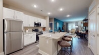 This single-floor residence is designed with a cohesive, modern aesthetic highlighted by wood-look flooring, neutral warm-toned walls, and bold teal accent walls that add a distinctive character to the living and bedroom areas. The open-concept kitchen flows seamlessly into the living space, making it ideal for everyday living and entertaining. The kitchen is outfitted with crisp white shaker cabinetry, light granite countertops, stainless steel appliances including a refrigerator, electric range, microwave, and dishwasher, and a central island with an undermount sink and bar seating for casual dining. Recessed lighting throughout the kitchen ensures a bright, functional workspace.

The living area accommodates comfortable furnishings and receives natural light through large windows. Each bedroom features a teal accent wall, window with exterior views, and direct access to a dedicated walk-in closet equipped with wire shelving systems offering substantial storage capacity. Both bathrooms mirror the kitchen's design language, featuring white vanity cabinetry, granite countertops, wood-look flooring, and a tub-shower combination. The overall layout is efficient and well-appointed, delivering a polished, contemporary living environment.