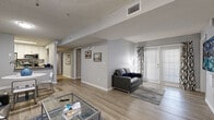 Located at 14525 Prism Circle in Tampa, FL, this single-floor unit offers a well-designed, functional layout across a generous footprint. The open living and dining area is anchored by light wood-look flooring, neutral gray walls, and large glass doors that invite abundant natural light. A glass-top coffee table and leather sofa create a comfortable gathering space, while the dining area sits adjacent for easy flow between the two zones.

The galley-style kitchen features white cabinetry with modern hardware, gray countertops, a deep stainless steel sink, and a full suite of stainless steel appliances including a refrigerator, electric range, microwave, and dishwasher. A soft blue accent wall adds a touch of personality to the space.

The bedrooms are well-appointed, each with wood-look flooring, window treatments providing privacy and light control, and ample room for both sleeping and working. One bedroom features a warm rose-toned accent wall with decorative wall art, adding a distinct character to the room.

Two bathrooms serve the unit, each finished with white cabinetry, framed mirrors, and light tile flooring. A dedicated in-unit laundry area houses a full-size washer and dryer with overhead shelving, adding everyday convenience. The overall aesthetic is clean, modern, and move-in ready.