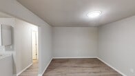 This single-floor unit offers a straightforward, well-maintained layout designed for comfortable everyday living. Consistent light wood-style laminate flooring runs throughout the space, complemented by neutral gray-beige walls and clean white baseboards, creating a cohesive and move-in-ready aesthetic.

The living area is open and adequately sized, receiving natural light through windows fitted with white horizontal blinds. A wall-mounted PTAC unit provides climate control, and a front entry door with a side window adds both accessibility and additional natural light to the main living space.

The kitchen is efficiently arranged in an L-shaped configuration, featuring white shaker-style cabinetry offering generous storage above and below the counters. A granite-look laminate countertop ties the space together, accompanied by a double stainless steel sink and a white electric coil range with an under-cabinet ventilation hood. A white refrigerator completes the appliance package.

The bedrooms are comfortably proportioned, each equipped with a flush-mount ceiling light fixture and windows that allow natural views of surrounding greenery. The bathroom includes a full tub and shower combination with a white fiberglass surround. Overall, the unit presents a clean, functional environment with consistent finishes throughout.