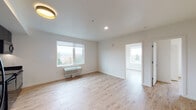 Located at 5620 N Interstate Ave in Portland, Oregon, this thoughtfully designed single-floor unit offers a clean, modern aesthetic throughout. Light wood-tone flooring runs continuously across the main living areas and bedrooms, creating a warm and cohesive feel that contrasts stylishly with the darker design elements found in the kitchen and bathrooms.

The open living area is bright and airy, featuring large windows that frame views of the surrounding Portland neighborhood and tree-lined landscape. A wall-mounted HVAC unit provides climate control, and recessed and flush-mount lighting fixtures illuminate the space efficiently.

The kitchen is outfitted with dark cabinetry extending to the ceiling, dark stone countertops, a matte black pull-down faucet, and a full suite of stainless steel and black appliances including an electric range, dishwasher, refrigerator, and over-the-range microwave — offering both functionality and a bold design statement.

The bedroom features a generous window with panoramic views and includes a built-in closet with a clothing rod. An additional secondary room provides flexible space with its own window and wall-mounted fixtures.

The bathroom is finished with dark tile flooring, a dark-cabineted vanity with an undermount sink, a large mirror, and a full soaking tub with a curved rod and matte black hardware — delivering a polished, contemporary finish throughout.
