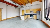 Located at 1110 Washington Ave in the heart of downtown St. Louis, this 2-bedroom, 2-bathroom loft showcases a striking industrial aesthetic with authentic architectural character. The open-concept living, dining, and kitchen area is anchored by soaring exposed wood-beam ceilings with visible ductwork and a polished concrete floor that flows throughout the entire space. Large, black-framed windows flood the interior with natural light and frame views of the surrounding urban skyline.

The kitchen is well-appointed with light maple cabinetry, dark countertops, stainless steel appliances including a refrigerator, range, microwave, and dishwasher, and a central island with a sink — ideal for both cooking and casual dining. A ceiling fan with track lighting adds to the functional yet stylish feel of the main living area.

Both bedrooms continue the loft's design language with concrete floors, exposed beam ceilings, and generous windows offering city views. The spacious primary bedroom includes an en-suite bathroom. Each bathroom features wood-toned vanities with dark countertops, white tile tub-shower combinations, and black hardware accents. Additional storage is provided by four closets throughout the unit. A narrow hallway with exposed ceiling joinery connects the private areas of the home.