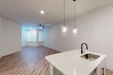 Located in Spring, TX, this thoughtfully designed single-story home offers a clean, modern aesthetic throughout its well-appointed layout. The open-concept kitchen and living area serves as the heart of the home, featuring light wood-tone luxury vinyl plank flooring that flows seamlessly through every room. The kitchen is a standout, equipped with stainless steel appliances including a range, microwave, and refrigerator, complemented by white cabinetry, a white quartz-topped island with an undermount sink and matte black faucet, and stylish pendant lighting overhead. The living area is bright and spacious, benefiting from natural light through windows dressed with horizontal blinds and a ceiling fan for year-round comfort. The generously sized primary bedroom continues the same flooring and neutral palette, with a ceiling fan, natural light from a corner window, and access to a dedicated walk-in closet outfitted with multi-level wire shelving for ample storage. The bathroom features a soaking tub with a tiled surround and matte black fixtures. A dedicated laundry room houses a full-size top-loading washer and dryer with overhead shelving, adding everyday convenience to this well-rounded home.