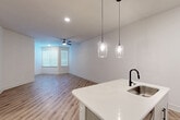 Located in Spring, TX, this thoughtfully designed single-story home offers a clean, modern aesthetic throughout its well-appointed layout. The open-concept kitchen and living area serves as the heart of the home, featuring light wood-tone luxury vinyl plank flooring that flows seamlessly through every room. The kitchen is a standout, equipped with stainless steel appliances including a range, microwave, and refrigerator, complemented by white cabinetry, a white quartz-topped island with an undermount sink and matte black faucet, and stylish pendant lighting overhead. The living area is bright and spacious, benefiting from natural light through windows dressed with horizontal blinds and a ceiling fan for year-round comfort. The generously sized primary bedroom continues the same flooring and neutral palette, with a ceiling fan, natural light from a corner window, and access to a dedicated walk-in closet outfitted with multi-level wire shelving for ample storage. The bathroom features a soaking tub with a tiled surround and matte black fixtures. A dedicated laundry room houses a full-size top-loading washer and dryer with overhead shelving, adding everyday convenience to this well-rounded home.