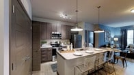 The Henry at Fritz Farms presents a stylish, single-floor residence designed with modern living in mind. The open-concept layout creates a seamless flow between the kitchen and living areas, making the space feel expansive and inviting. The kitchen is a standout feature, showcasing rich dark wood cabinetry, granite countertops, and a full suite of stainless steel appliances, including a range, microwave, and refrigerator. A large kitchen island with a built-in sink serves as both a functional workspace and a casual dining area, complemented by contemporary pendant lighting that adds a warm, stylish glow. Track lighting above the main kitchen workspace ensures excellent illumination throughout. The light wood-style flooring runs throughout the space, contributing to a clean and cohesive aesthetic. The open sightlines from the kitchen into the adjoining living and dining areas reinforce the airy, connected feel of the floor plan. Subtle accent wall colors add a touch of personality without overwhelming the modern palette. Overall, the space combines functional design with upscale finishes, offering a comfortable and contemporary environment at The Henry at Fritz Farms.