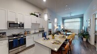 This thoughtfully designed single-floor residence combines contemporary style with functional living. The open-concept kitchen is a standout feature, boasting crisp white shaker cabinetry extending to soaring ceilings, granite countertops, a classic subway tile backsplash, and a full suite of stainless steel appliances. A generously sized center island with seating serves as both a dining and gathering hub, illuminated by elegant pendant lighting overhead. The kitchen flows seamlessly into the dining area and living room, where large windows and a glass door to the balcony invite abundant natural light and outdoor views. The living area offers elevated ceilings and warm hardwood-style flooring throughout the main spaces. Two well-sized bedrooms provide comfortable retreats, each featuring plush carpeting, large windows dressed with blinds and curtains, and ample room for furnishings. Both bathrooms are finished with granite-topped vanities, undermount sinks, and dark-framed mirrors. The primary bathroom features a glass-enclosed shower and direct access to a walk-in closet. The secondary bathroom similarly connects conveniently to its adjacent bedroom. Together, these spaces create a cohesive, modern living environment with a clean, neutral palette and high-quality finishes throughout.