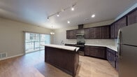 Located at 1605 Meijer Dr in Greenville, Michigan, this single-floor 1-bedroom, 1-bathroom unit offers a thoughtfully designed open-concept layout finished with contemporary details throughout. The kitchen is a standout feature, showcasing rich dark espresso cabinetry reaching toward the ceiling, quartz countertops with elegant veining, a classic subway tile backsplash, and a full suite of stainless steel appliances including a range, microwave, and refrigerator. A large center island with additional quartz countertop space and a built-in sink serves as both a functional workspace and a natural divider between the kitchen and living area. Track lighting and a pendant chandelier provide layered illumination throughout. The spacious living area features warm wood-look flooring, a ceiling fan, and a sliding glass door that opens to a private balcony, inviting natural light and outdoor views. The bedroom offers generous closet storage with double closet doors, complemented by the same warm flooring found throughout the unit. The bathroom is well-appointed with dark wood vanity cabinetry, a quartz-topped single sink vanity, a large mirror, and accessibility grab bars, all set on durable wood-look flooring.