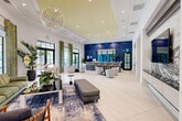 Located at 11181 W 35th Way in Hialeah, Florida, this single-floor community clubhouse delivers a sophisticated and welcoming atmosphere through thoughtful architectural design and high-end finishes. The expansive open-plan interior is anchored by large-format porcelain tile flooring and soaring ceilings, with a coffered tray ceiling accent highlighted in warm yellow that draws the eye upward. A dramatic starburst chandelier serves as a centerpiece, casting ambient light across the lounge areas below.

The space is divided into distinct yet flowing zones. A comfortable lounge area features plush green sofas, eclectic accent chairs, and layered area rugs, framed by floor-to-ceiling black-framed windows dressed with bold green and gold patterned drapes that flood the interior with natural light. A separate seating zone with a vibrant blue sofa and yellow accent chairs sits beneath a striking decorative ceiling medallion with a botanical motif.

A built-in bar counter lined with high-backed stools is backed by an eye-catching deep-blue mosaic tile feature wall, providing an ideal social gathering spot. Nearby, a dedicated media wall showcases a large flat-screen television set against a dramatic full-slab marble surround with swirling grey and white veining. Lush tropical plants are thoughtfully placed throughout, reinforcing the Florida ambiance.