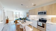 Located in Bethesda, MD, this thoughtfully designed 2-bedroom, 1-bathroom unit offers a modern, open-concept layout with clean lines and contemporary finishes throughout. The kitchen and living area flow seamlessly together, anchored by a sleek kitchen featuring light wood upper cabinetry, white lower cabinets, a white tile backsplash, stainless steel appliances including a French door refrigerator, and a white waterfall-edge island that doubles as a dining space. Light wood-tone flooring runs throughout the main living area, enhancing the bright, airy atmosphere. The living room is bathed in natural light from large floor-to-ceiling windows that frame open outdoor views, creating a welcoming and spacious feel. The primary bedroom continues the modern aesthetic with soft carpeting, a generous walk-in closet with built-in shelving, and a large window that fills the room with natural light. The second bedroom also benefits from a bright window and neutral finishes. The bathroom features a full soaking tub and shower combination, a wood-toned vanity with a white countertop, and clean tile flooring. Throughout the unit, white walls, recessed lighting, and carefully considered details contribute to a cohesive, contemporary living environment.