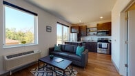 This single-floor unit offers a thoughtfully designed open-concept layout that seamlessly connects the living area and kitchen. The living space features warm hardwood-style flooring, a dark leather sofa with teal accent pillows, a patterned area rug, and a dedicated workspace with a wooden desk — providing both comfort and functionality. Large windows throughout flood the space with abundant natural light and offer pleasant views of the surrounding tree-lined neighborhood.

The kitchen is well-equipped with dark espresso cabinetry, granite-style countertops, and a full suite of stainless steel appliances, including a refrigerator, dishwasher, electric range, and built-in microwave. A peninsula counter serves as a natural divider between the kitchen and living area, adding extra prep and dining space.

The bedroom is a bright, airy retreat with multiple large windows on two walls, allowing natural light to pour in from multiple angles while framing views of the surrounding neighborhood. Carpet flooring adds warmth underfoot.

The bathroom maintains a clean, modern aesthetic with hardwood-style flooring, a dark-cabinetry vanity with a white countertop, and a full tub and shower combination. The overall design of the space is modern and cohesive, with neutral tones and practical finishes throughout.