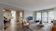 Located at 5805 Waxham Ct in Virginia Beach, Virginia, this single-floor residence offers a well-designed layout with a cohesive, contemporary aesthetic throughout. The living room serves as the heart of the home, featuring crown molding, wood-look flooring, and a large sliding glass door that floods the space with natural light and provides direct access to an outdoor patio with greenery views. The kitchen is outfitted with white shaker-style cabinetry, black hardware accents, light quartz countertops, and stainless steel appliances including a gas range and refrigerator. A stacked washer and dryer unit is conveniently integrated into the kitchen area. An adjacent flex space functions well as a dining area or home office, complete with a window and wood-look flooring. The bedrooms are carpeted for comfort, each featuring neutral tones, natural light from well-placed windows, and ample space for furnishings. The bathrooms are finished with wood-look tile flooring, white vanities with black hardware, and clean, minimal styling. Neutral wall tones, consistent flooring materials, and thoughtful detailing create a unified and functional living environment throughout this Virginia Beach home.