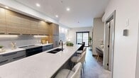 Located at 8 Mission Rd SW in Calgary, this thoughtfully designed one-bedroom, one-bathroom unit offers a contemporary open-concept layout that maximizes its compact footprint. The kitchen is a standout feature, boasting an elongated quartz waterfall island with bar seating, two-tone cabinetry combining warm wood-grain uppers with slate-grey lowers, under-cabinet lighting, black stainless appliances including a French door refrigerator, and a matte black faucet over a deep undermount sink. The kitchen flows seamlessly into the living area, which is bathed in natural light from a large sliding glass door that opens to a private balcony, offering outdoor views. The living room provides a comfortable, well-proportioned space with recessed lighting and neutral warm-toned walls. The bedroom accommodates a full-sized bed and features a large sliding window that draws in ample natural light. The bathroom is finished to a high standard with large-format tile surround, a soaker tub with rain shower, a floating grey vanity with a white countertop, and a backlit wood-niche accent shelf. A dedicated closet completes the layout. Consistent tile flooring, recessed lighting, and a cohesive grey and natural wood palette throughout give this unit a refined, modern aesthetic.
