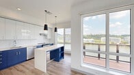 Located along the South Side waterfront at 2695 S Water St in Pittsburgh, PA, this modern 2-bedroom, 1-bathroom residence offers a thoughtfully designed single-floor layout with a clean, contemporary aesthetic throughout. Light hardwood-style flooring flows seamlessly across every room, complementing the crisp white walls and bright, airy atmosphere.

The kitchen is a standout feature, showcasing a bold two-tone design with white upper cabinetry and navy blue lower cabinets, a white subway tile backsplash, stainless steel appliances, and a matching navy and white island with open shelving. Dual pendant lights hang above, while large floor-to-ceiling windows frame sweeping views of the river and surrounding hillside.

The primary bedroom is generously sized, bathed in natural light from oversized windows that offer views of the surrounding neighborhood and lush hillsides. A well-appointed walk-in closet features wire shelving along multiple walls, providing ample storage. The second bedroom is bright and functional, with light-filled windows and access to the hallway. A central corridor connects all rooms cleanly.

The bathroom is finished in a modern style with a frameless glass walk-in shower, white vanity with a clean countertop, and wood-look tile flooring. Recessed lighting adds a polished touch. An outdoor balcony accessible from the main living area rounds out this well-appointed urban residence.