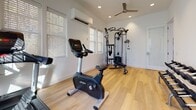 Located at 260 Pidgeon Bay Rd in Summerville, SC, this dedicated single-floor fitness studio is thoughtfully designed to deliver a comprehensive workout experience in a clean, well-appointed setting. The space features light hardwood flooring throughout, crisp white walls, and recessed lighting complemented by a ceiling fan, creating a bright and energizing atmosphere.

Natural light flows in through multiple windows dressed with white blinds, keeping the environment airy and comfortable. A wall-mounted mini-split unit provides dedicated climate control, ensuring year-round comfort during workouts.

The studio is outfitted with professional-grade Life Fitness equipment, including a stationary upright bike, a treadmill, and a dual-cable functional trainer complete with a weight stack and adjustable bench — ideal for a wide range of strength and conditioning exercises. A fully stocked two-tier dumbbell rack lines one wall, offering a broad selection of free weights to support varied training routines. A yoga or exercise mat is also conveniently stored along the wall for flexibility and floor work.

The open floor plan provides ample space to move freely between equipment, while the overall design maintains a clean, uncluttered aesthetic. This private fitness studio offers an exceptional facility for health-focused use.