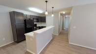 This contemporary apartment showcases a thoughtfully designed open floor plan that maximizes space and functionality. The heart of the home is a sleek, updated kitchen featuring dark wood cabinetry, black appliances, and a convenient breakfast bar that overlooks the living area. The kitchen's modern aesthetic is complemented by pendant lighting and a mix of ambient and task lighting.

Throughout the apartment, light-toned laminate flooring creates a seamless flow between spaces, enhancing the sense of openness. The neutral color palette, predominantly in shades of white and light gray, contributes to a bright and airy ambiance. Large windows in the bedrooms and living areas allow for ample natural light and are fitted with horizontal blinds for privacy control.

The bathroom is efficiently designed with a white fixtures, including a combined bathtub and shower unit. The space is finished with clean lines and minimalist hardware, maintaining the modern aesthetic found throughout the apartment.

Bedrooms are generously sized and feature ceiling fans for comfort. The overall layout, as seen in the 3D floor plan, indicates a well-thought-out design that balances private and communal spaces. This apartment offers a contemporary living experience with its updated features, neutral decor, and emphasis on natural light and open space.