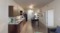 This single-floor unit offers a well-organized layout that accommodates multiple residents comfortably. The kitchen is a functional centerpiece, featuring rich dark wood cabinetry, granite-style countertops, stainless steel appliances including a dishwasher, microwave, and range, along with ample upper and lower cabinet storage. Wood-style flooring runs through the kitchen and common areas, adding warmth to the space.

The living area provides room for a sectional sofa and is characterized by neutral walls, window blinds for light control, and exposed industrial-style ductwork that adds a modern edge to the design. A dedicated dining space with a bar-height table is conveniently positioned near the kitchen, and in-unit washer and dryer hookups are visibly integrated into the common area.

Multiple bedrooms offer carpeted flooring, natural light from windows with blinds, and built-in closets with hanging rods and drawer storage. The rooms comfortably accommodate a bed and desk setup, making them well-suited for student living.

Two bathrooms serve the unit, each finished with tile flooring, granite-top vanities with undermount sinks, and tub-shower combinations, providing practical, well-appointed facilities for daily use.
