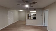 This single-floor residence offers a clean, functional layout designed for comfortable everyday living. The open-concept living area is finished with warm-toned wood-look flooring and neutral walls, creating a bright and cohesive atmosphere. A ceiling fan provides both lighting and ventilation overhead, while the space flows seamlessly toward the pass-through kitchen. The kitchen is well-equipped with a full suite of stainless steel appliances, including a refrigerator, range with microwave above, and dishwasher. White shaker-style cabinetry lines the walls, complemented by a skylight that brings in natural overhead light, and a breakfast bar counter separates the kitchen from the living area. A dedicated bedroom offers a comfortable retreat, featuring wood-look flooring, a ceiling fan with light, and a window with blinds that invites natural light and outdoor views. The full bathroom includes a tiled shower-tub combination, a vanity with a gray countertop, and a textured ceiling. A separate laundry room accommodates a full-size top-loading washer and dryer with overhead shelving for added storage. Throughout the space, consistent flooring, clean white trim, and a neutral color palette create a unified, move-in-ready environment.