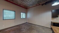 Located along US-36 E in Elwood, Kansas, this single-floor space offers a compelling blend of industrial character and functional amenities. The main open area is defined by its raw, exposed ceiling with visible weathered texturing, red-painted structural beams, and industrial piping running overhead, lending the space a distinct urban aesthetic. Concrete floors throughout reinforce the industrial feel while providing a durable, low-maintenance surface.

Multiple windows fitted with horizontal blinds allow natural light to filter into the main area, brightening the neutral-toned walls and creating a welcoming atmosphere despite the rugged architectural elements. Vertical pipe columns punctuate the open layout, contributing to the space's character.

The kitchenette is well-equipped with matte black upper and lower cabinetry, a double stainless steel sink, warm wood-toned countertops, and a full-size refrigerator, along with an electrical panel conveniently located on the wall. The polished concrete floors continue seamlessly into this functional area.

The bathroom offers a clean, modern contrast to the industrial surroundings, featuring a striking blue vessel sink atop a dark vanity with a stone-look countertop, a full tub and shower combination with grab bars, and bright chrome fixtures. Pendant and overhead lighting complete the practical, well-appointed interior.
