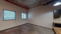 Located along US-36 E in Elwood, Kansas, this single-floor space offers a compelling blend of industrial character and functional amenities. The main open area is defined by its raw, exposed ceiling with visible weathered texturing, red-painted structural beams, and industrial piping running overhead, lending the space a distinct urban aesthetic. Concrete floors throughout reinforce the industrial feel while providing a durable, low-maintenance surface.

Multiple windows fitted with horizontal blinds allow natural light to filter into the main area, brightening the neutral-toned walls and creating a welcoming atmosphere despite the rugged architectural elements. Vertical pipe columns punctuate the open layout, contributing to the space's character.

The kitchenette is well-equipped with matte black upper and lower cabinetry, a double stainless steel sink, warm wood-toned countertops, and a full-size refrigerator, along with an electrical panel conveniently located on the wall. The polished concrete floors continue seamlessly into this functional area.

The bathroom offers a clean, modern contrast to the industrial surroundings, featuring a striking blue vessel sink atop a dark vanity with a stone-look countertop, a full tub and shower combination with grab bars, and bright chrome fixtures. Pendant and overhead lighting complete the practical, well-appointed interior.