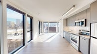 Located on the sixth floor at 1315 NW Johnson Street in Portland's vibrant Pearl District, unit 609 is a modern, thoughtfully designed residence that blends clean architectural lines with an abundance of natural light. Light-toned hardwood flooring runs throughout the space, complementing the crisp white walls and creating a bright, cohesive aesthetic.

The open-concept living and kitchen area is the heart of the unit, anchored by expansive floor-to-ceiling windows on multiple sides that flood the interior with sunlight and frame sweeping views of the Portland cityscape. The kitchen is outfitted with sleek grey cabinetry, stainless steel appliances including a dishwasher, range, microwave, and refrigerator, as well as light countertops and a single-basin sink — a functional and stylish galley-style setup.

The living area is generously proportioned, with large sliding glass doors and picture windows offering panoramic urban views, creating an airy, loft-like atmosphere. A dedicated hallway leads to additional rooms, including a full bathroom featuring a soaking tub and shower combination with wood-toned flooring and clean white finishes. A convenient in-unit stacked washer and dryer is neatly tucked behind louvered closet doors, adding everyday practicality to this well-appointed urban residence.