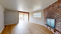 Located at 6000-6122 N Jefferson St in Kansas City, MO, this 1-bedroom, 2-bathroom single-floor residence offers a thoughtfully arranged layout across two living areas, a kitchen, hallway, and a well-appointed bedroom. The main living room is a standout space, featuring a full brick fireplace, exposed wood beam accents, a textured ceiling, and light hardwood-style flooring that extends throughout the common areas. Large windows invite generous natural light, and a sliding glass door opens to a private patio, seamlessly connecting indoor and outdoor living. A second living area, also with hardwood-style flooring, provides flexible space for dining or a home office and connects directly to the kitchen. The kitchen includes white cabinetry with brass hardware, dark countertops, and standard appliances. The bedroom is carpeted for comfort, features a ceiling fan with light, a window for natural light, and a closet. Both bathrooms are finished with dark countertop vanities, white cabinetry, and one includes a tub/shower combination with a window above. The hallway bathroom features a broad vanity with a large mirror and Hollywood-style lighting. The overall aesthetic is clean and neutral, offering a comfortable and functional living environment.