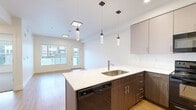 This well-appointed one-bedroom, one-bathroom unit at 450 State Street in Clearfield, Utah offers a thoughtfully designed single-floor layout that maximizes every square foot. The open-concept kitchen is a standout feature, showcasing two-tone cabinetry with dark lower and light upper cabinets, white quartz countertops, and a large peninsula with an integrated sink and seating — ideal for casual dining or entertaining. Black stainless appliances, including a refrigerator, range, and microwave, complement the modern aesthetic, while pendant lighting adds a stylish finishing touch. Light-toned hardwood-style flooring flows throughout the main living areas, creating a bright and cohesive feel. The spacious bedroom offers plush carpeting, a large window with outdoor views, and a tray ceiling detail that adds architectural character. The full bathroom continues the modern design language with a wood-toned vanity, white quartz countertop, and a full tub and shower combo with built-in shelving. A dedicated laundry area with an included washer and dryer hookups adds everyday convenience. A closet and hallway complete the functional layout of this clean, contemporary unit.