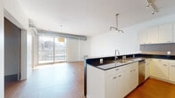 Located in Minneapolis's vibrant North Loop neighborhood, this modern unit at 915 Washington Ave N offers a well-designed single-floor layout encompassing a comfortable amount of living space. The open-concept kitchen and living area serves as the heart of the unit, featuring a sleek peninsula with dark granite countertops, white cabinetry, stainless steel appliances including a gas range and refrigerator, and track lighting overhead. Warm-toned bamboo hardwood flooring extends throughout the main living areas, adding a natural richness to the contemporary aesthetic. Exposed cylindrical ductwork running along the ceiling lends an industrial-modern character to the space. The living room is bathed in natural light thanks to expansive floor-to-ceiling sliding glass doors that open to a private balcony with views of the surrounding Minneapolis cityscape. The unit includes two bathrooms: one featuring a full soaking tub and shower combo with tile flooring, and a second, more spacious bathroom with dual sinks set in dark granite countertops, a walk-in shower, and illuminated mirrors. Two hallways provide efficient circulation throughout the unit, connecting all areas seamlessly. The clean white walls and bright, light-filled interiors create an airy and inviting urban living environment.