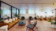 This thoughtfully designed single-floor space blends fitness, relaxation, and social amenities into a cohesive, modern environment. The layout flows seamlessly across distinct zones, each serving a specific purpose while maintaining a unified aesthetic defined by light wood flooring, neutral tones, and contemporary furnishings.

The fitness area is well-appointed with a cable weight machine, kettlebell rack stocked with a full range of weights, medicine balls, and a rowing machine, all set on durable flooring with recessed lighting above. Roller-shaded windows allow soft, diffused light to fill the room while maintaining privacy.

Adjacent to the gym is an inviting lounge zone that offers generous seating through a mix of a camel-toned sofa, upholstered armchairs, and woven accent chairs arranged around low coffee tables. Tall potted plants and curated wall art add warmth and character throughout.

The kitchenette is a standout feature, complete with a white quartz bar counter, bar stools, a professional espresso machine, under-counter beverage refrigerators, and a classic subway tile backsplash — ideal for post-workout refreshment or casual socializing.

Throughout the space, consistent design choices — clean lines, layered greenery, and abundant ambient lighting — create a welcoming atmosphere that balances functionality with aesthetic appeal.