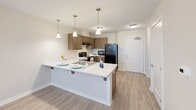 Located at 1455 Castle Manor Dr in Lincoln, Illinois, this single-floor residence offers a thoughtfully laid-out living space designed for comfort and functionality. The open-concept kitchen and living room serve as the heart of the home, where warm-toned cabinetry, white countertops, and a peninsula island with pendant lighting create an inviting and practical hub. The kitchen is fully equipped with black appliances including a range, refrigerator, and dishwasher, complemented by ample upper and lower cabinet storage and a dedicated pantry. Light wood-look flooring flows throughout the main living area, enhancing the bright, airy feel provided by natural light from well-placed windows. A ceiling fan in the living area adds both style and comfort. The bedroom is a comfortable retreat featuring plush carpeting, a ceiling fan, and a window that invites natural light. Three closets throughout the unit provide generous storage solutions. The bathroom is clean and functional, featuring a tub-shower combination with a curtain, wood-look flooring, and accessibility-friendly grab bars. A utility room rounds out the layout, adding everyday convenience. The overall aesthetic is modern and neutral, with a clean palette that makes the space feel fresh and move-in ready.